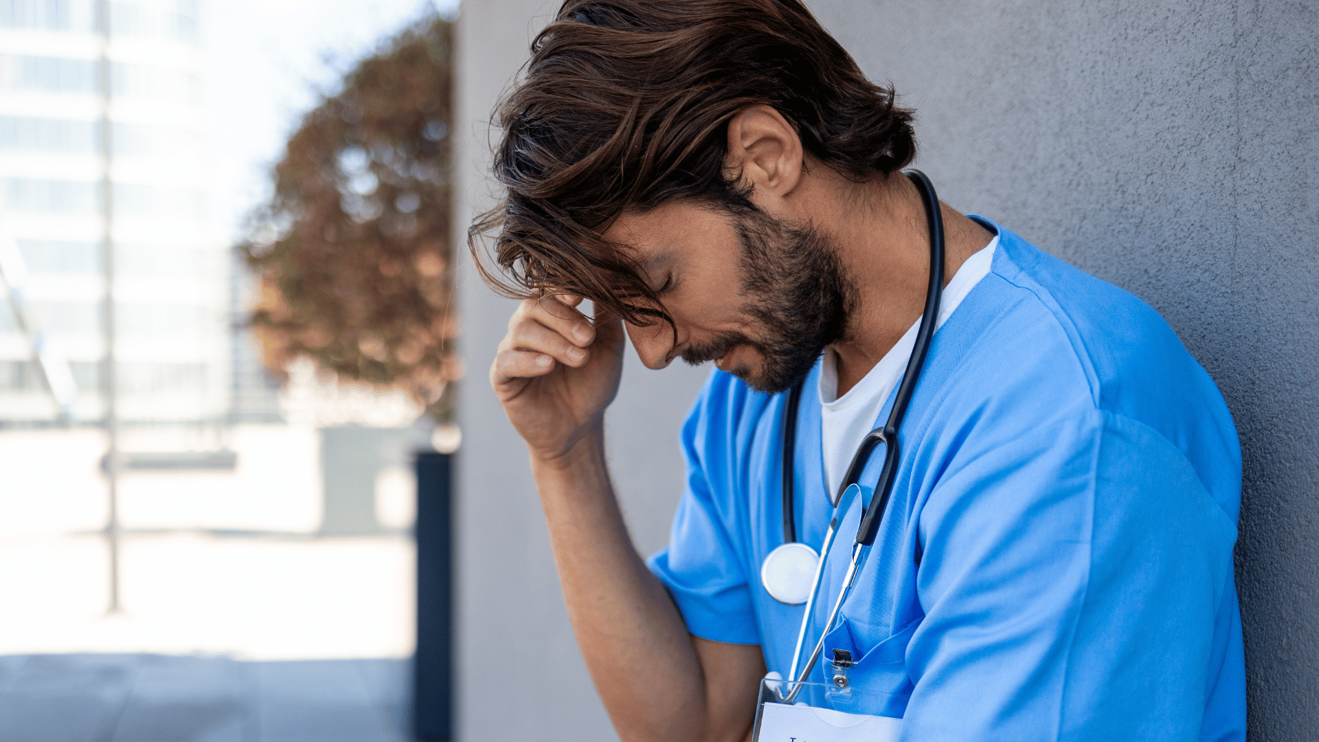male nurse showing signs of being overwhelmed while standing outside against a wall